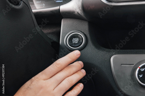 Closeup of a hand pressing a startstop button on a car's steering wheel, highlighting vehicle interior and modern technology features, emphasizing the convenience and innovation in automotive design photo