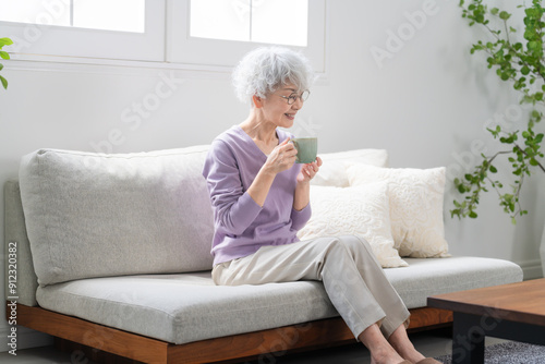 ソファーでコーヒーを飲みながらくつろぐシニア女性