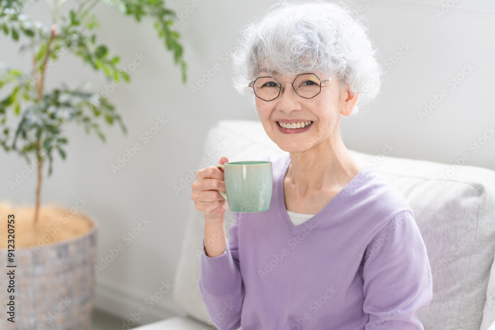 ソファーでコーヒーを飲みながらくつろぐシニア女性 ソファーでコーヒーを飲みながらくつろぐシニア女性