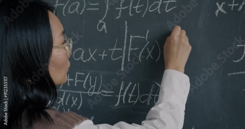 Intelligent Asian lady mathematician writing on chalkboard concentrated on science and maths. Academic education and master degree concept.