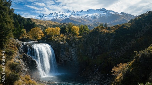 A picturesque waterfall in a mountainous region, with snow-capped peaks visible in the distance.
