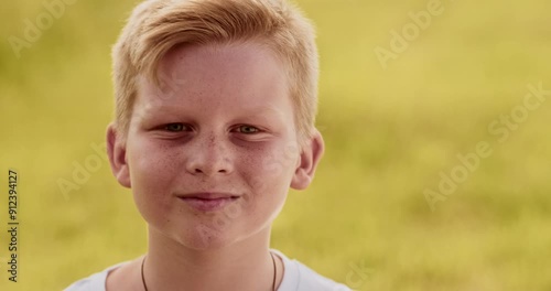 Close up portrait of young boy looking at camera. Non urban scene, windy day, yellow field, candid child enjoying beauty of nature, ukrainian teenager. High quality 4k footage