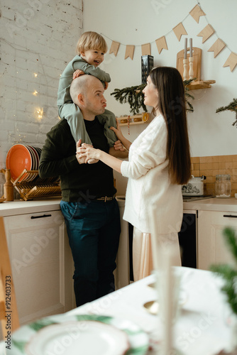A happy family. Happy young couple with their little son in the kitchen decorated for the new year. New Year's interior in the kitchen. Christmas kitchen. Festive family atmosphere.