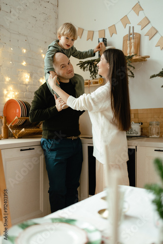 A happy family. Happy young couple with their little son in the kitchen decorated for the new year. New Year's interior in the kitchen. Christmas kitchen. Festive family atmosphere.