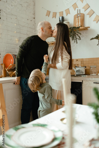 A happy family. Happy young couple with their little son in the kitchen decorated for the new year. New Year's interior in the kitchen. Christmas kitchen. Festive family atmosphere.