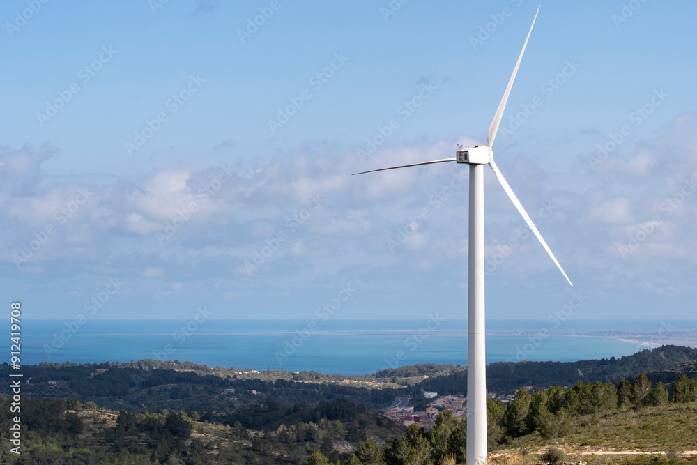 A solitary wind turbine stands by the tranquil sea boasting white clouds in the sky, representing sustainable energy and the harmony between technology and nature. A solitary wind turbine stands by the tranquil sea boasting white clouds in the sky, representing sustainable energy and the harmony between technology and nature.
