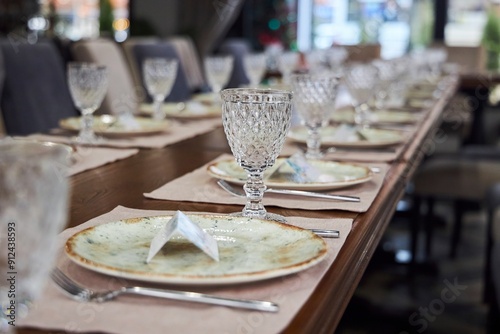 A table with a lot of glasses and plates with a napkin on the plate. The table is set for a dinner party