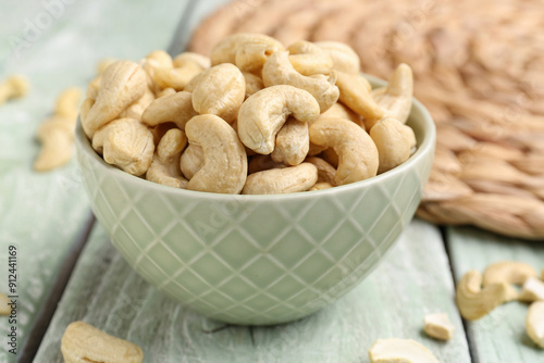 Bowl with tasty cashew nuts on light wooden background, closeup