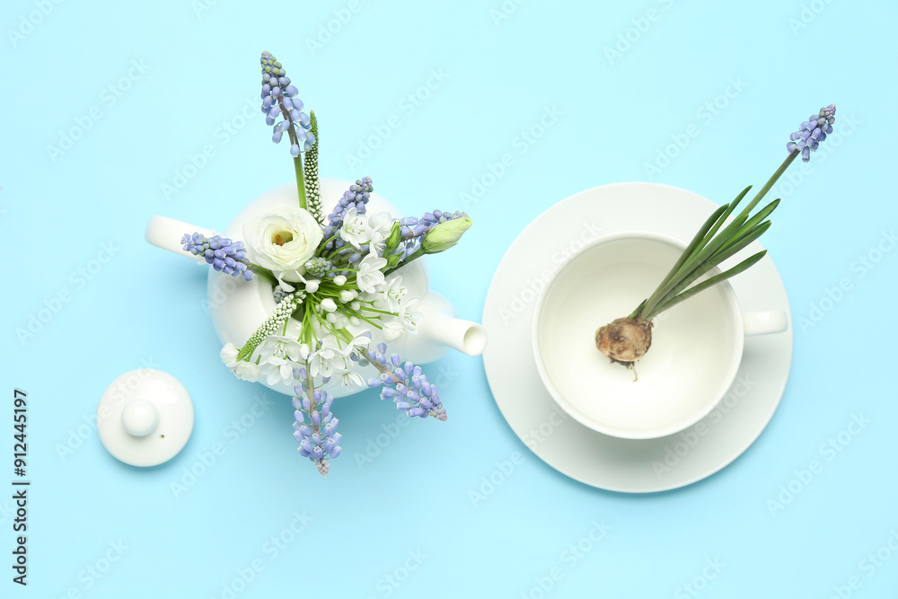 Composition with beautiful Muscari flowers in teapot and cup on blue background Composition with beautiful Muscari flowers in teapot and cup on blue background
