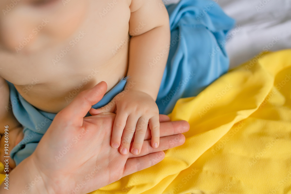 Fototapeta premium Baby Hand Holding Adult Hand with Ukrainian Flag Colors
