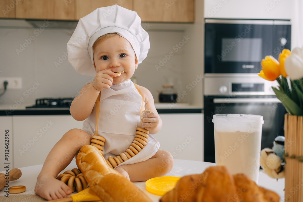 Cute Baby Chef Sitting on Kitchen Counter with Pastries and Fresh Bread Cute Baby Chef Sitting on Kitchen Counter with Pastries and Fresh Bread