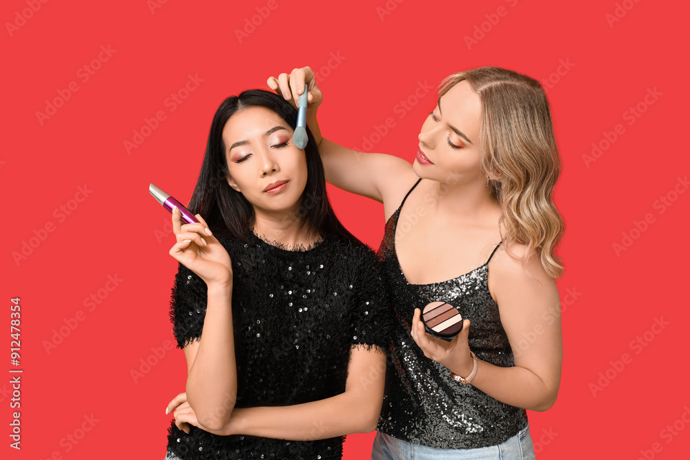 Pretty young women applying decorative cosmetics on red background Pretty young women applying decorative cosmetics on red background