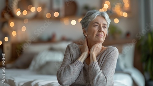 Senior woman sitting on her bed massaging her neck.