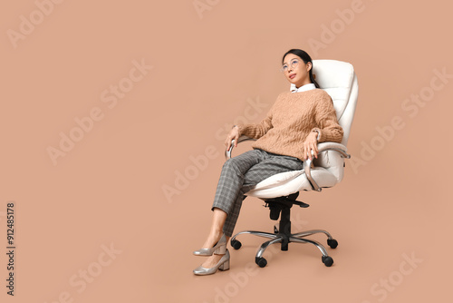 Portrait of young Asian businesswoman sitting on armchair against beige background