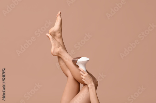 Obraz na plátne Legs of young woman with modern photoepilator on brown background