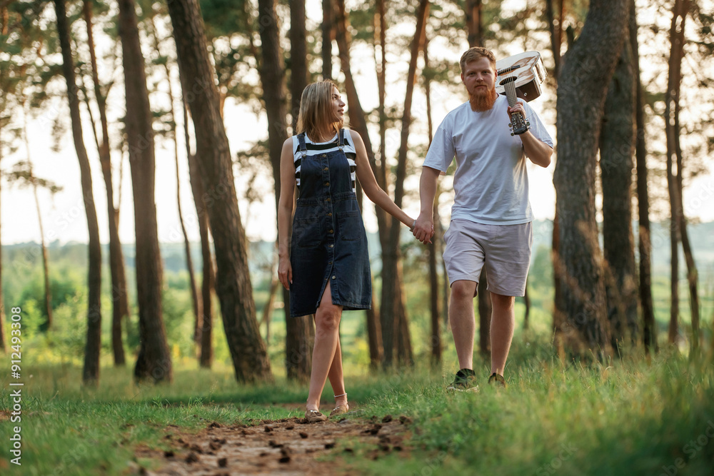 With acoustic guitar. Lovely couple are together in the forest at summer daytime With acoustic guitar. Lovely couple are together in the forest at summer daytime