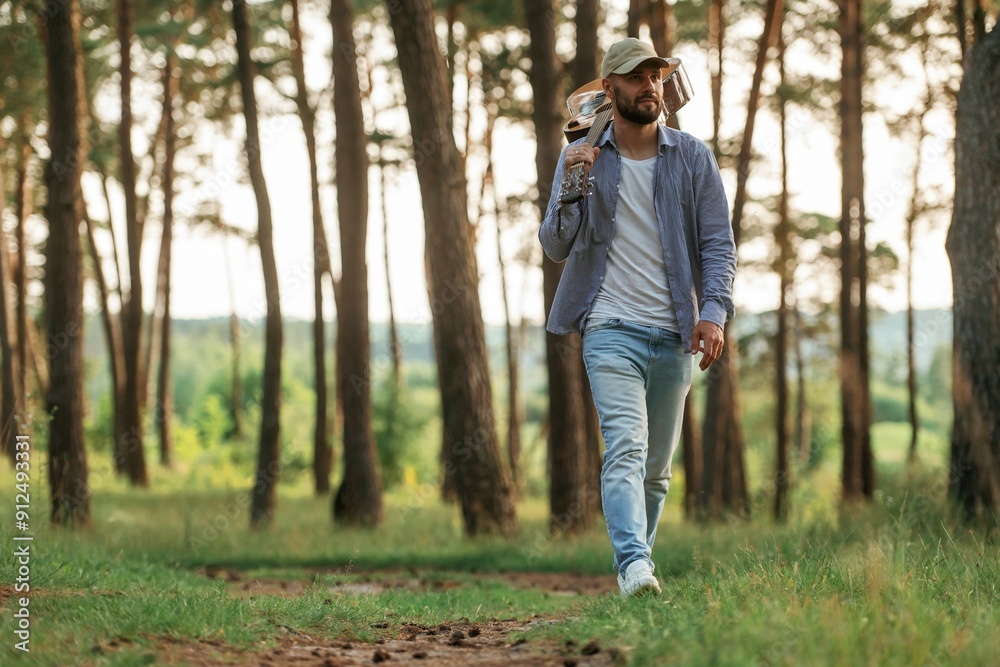 Walking forward. Handsome man is in the forest with acoustic guitar
