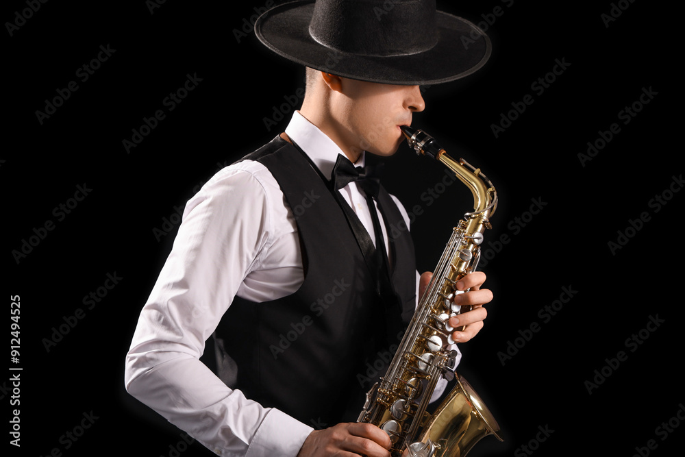 Fototapeta premium Male artist playing saxophone on black background