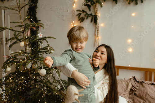 mother and son jump and have fun on the bed. the house is decorated for Christmas, Christmas tree and fir branches. New Year's decor
