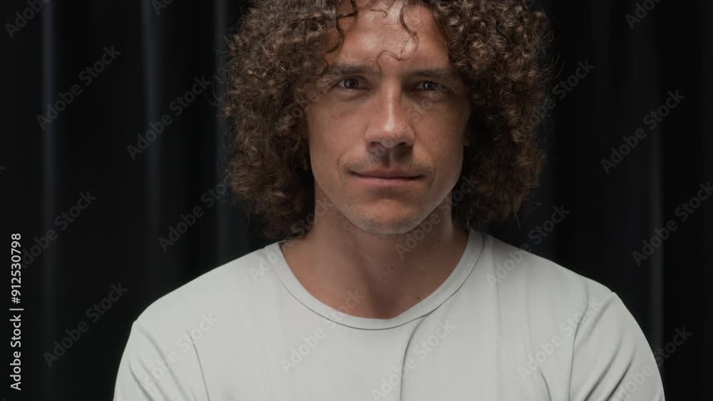 Tilt up portrait of handsome curly haired Caucasian man wearing white long sleeve on muscular body posing for camera with folded hands on black background Tilt up portrait of handsome curly haired Caucasian man wearing white long sleeve on muscular body posing for camera with folded hands on black background