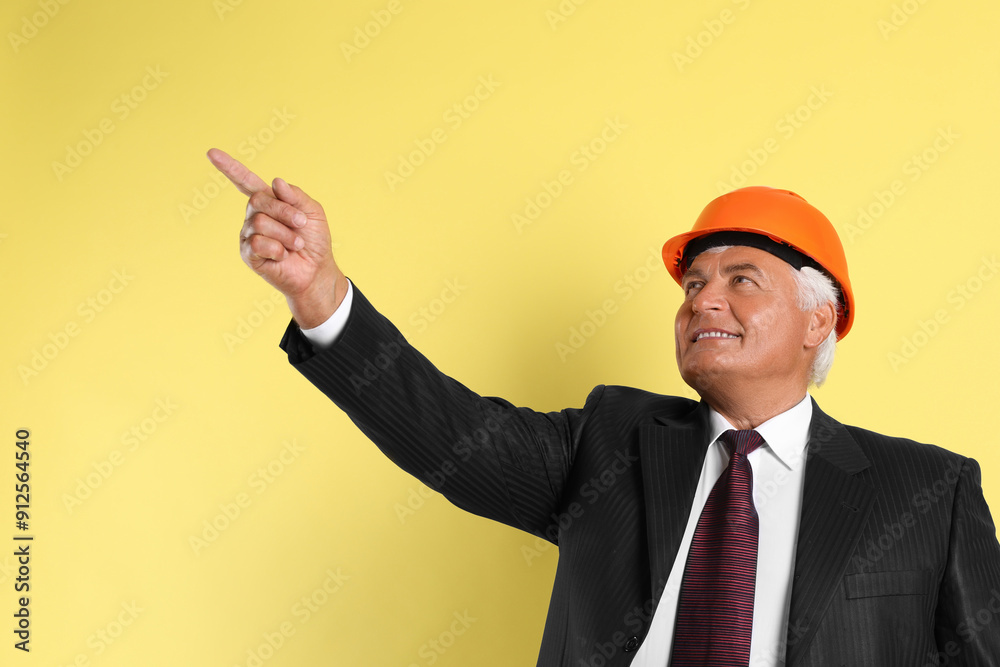 Engineer in hard hat pointing at something on yellow background Engineer in hard hat pointing at something on yellow background
