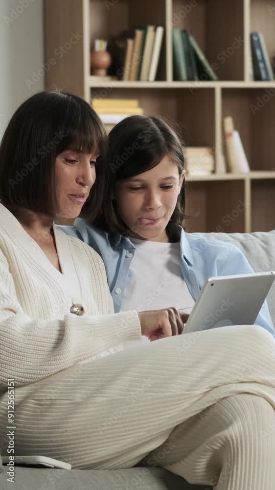 Cheerful Caucasian mother and teenage son spending leisure time online together using tablet computer, sitting on sofa at home. Vertical video. Cheerful Caucasian mother and teenage son spending leisure time online together using tablet computer, sitting on sofa at home. Vertical video.
