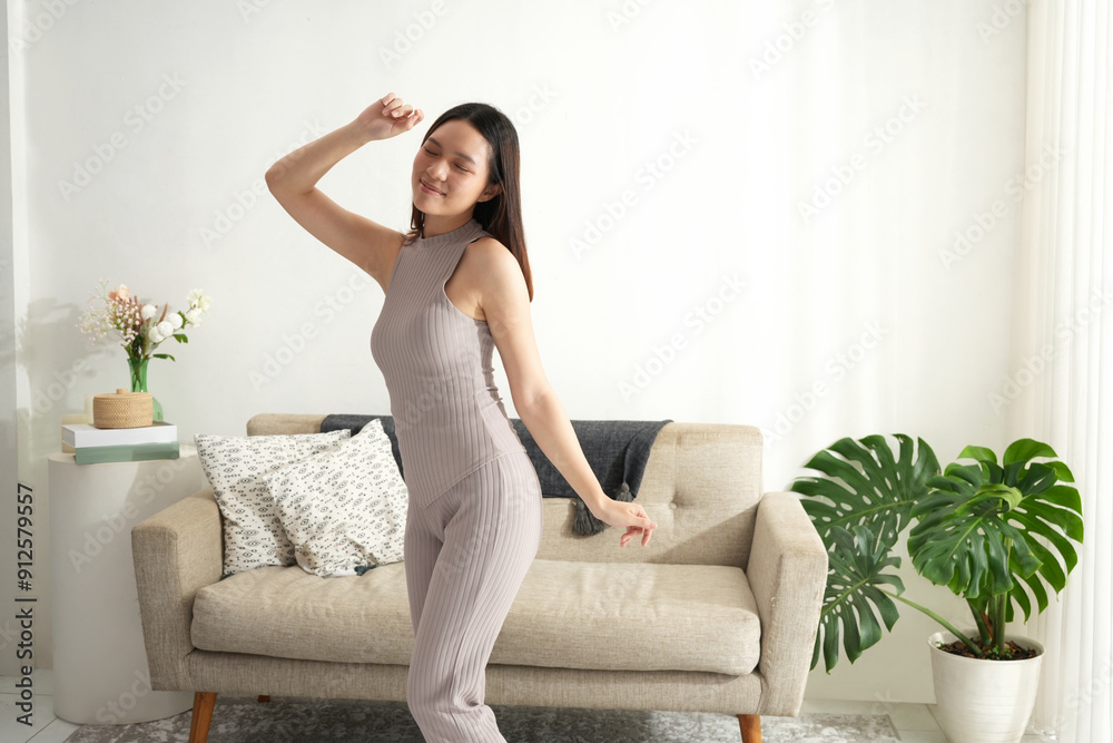 An Asian woman joyfully dances in front of her smartphone, recording content at home. She wears comfortable loungewear and smiles brightly, enjoying the moment in a cozy, well-lit living room. An Asian woman joyfully dances in front of her smartphone, recording content at home. She wears comfortable loungewear and smiles brightly, enjoying the moment in a cozy, well-lit living room.