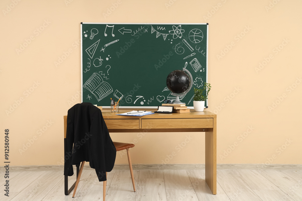 Obraz na plátně Teacher's table with school stationery and blackboard on beige wall in classroom