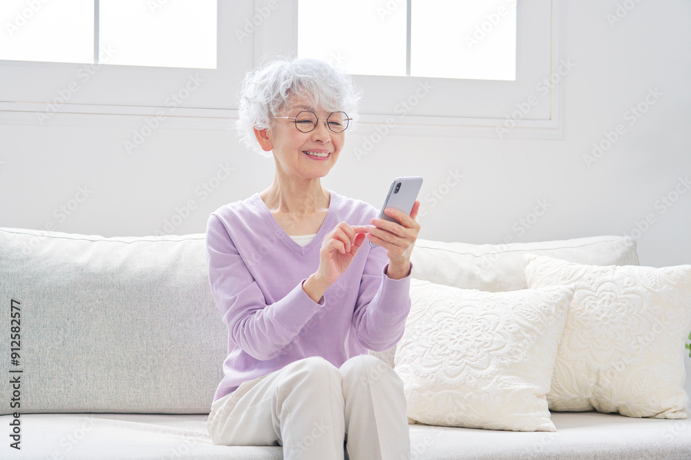 スマートフォンを使うシニア女性 リビングルーム スマートフォンを使うシニア女性 リビングルーム