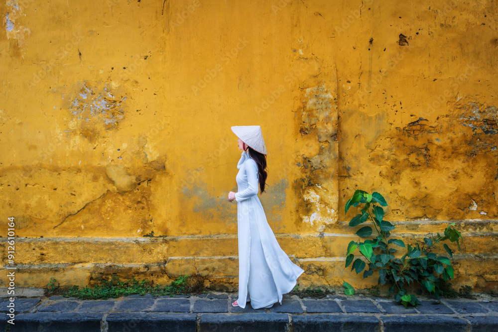 Asian woman wearing traditional Vietnamese culture walks beside an old wall in Hoi An, Vietnam. Asian woman wearing traditional Vietnamese culture walks beside an old wall in Hoi An, Vietnam.