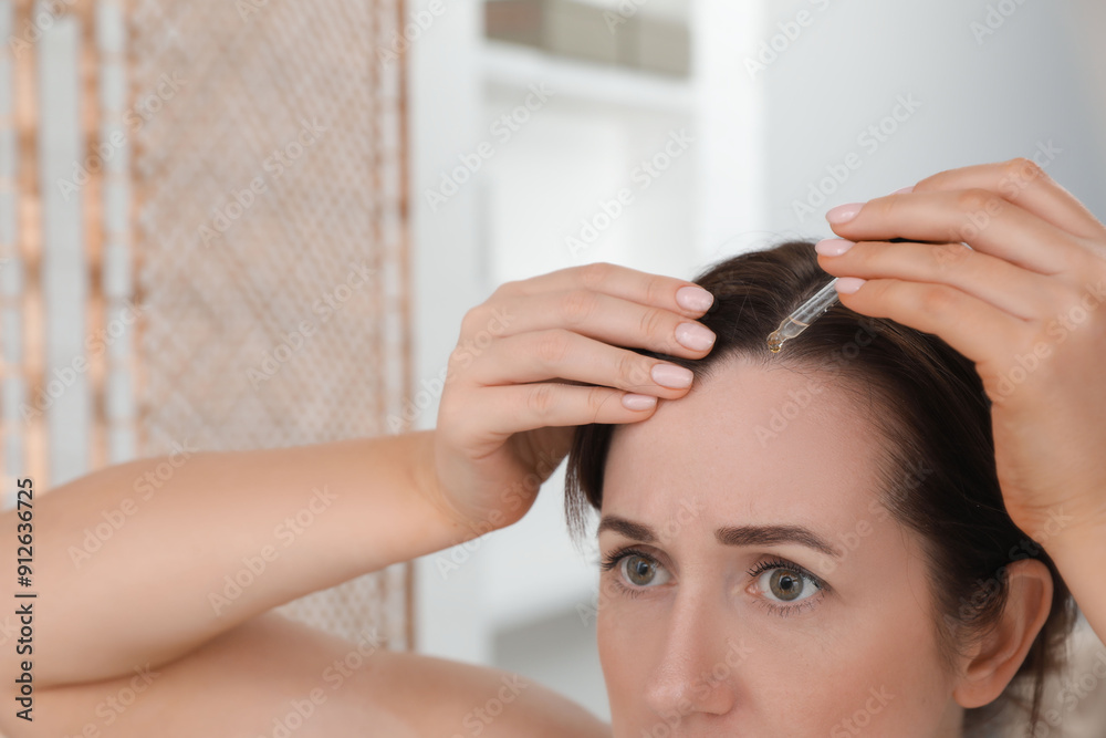 Naklejka premium Hair loss problem. Woman applying serum onto hairline indoors, closeup