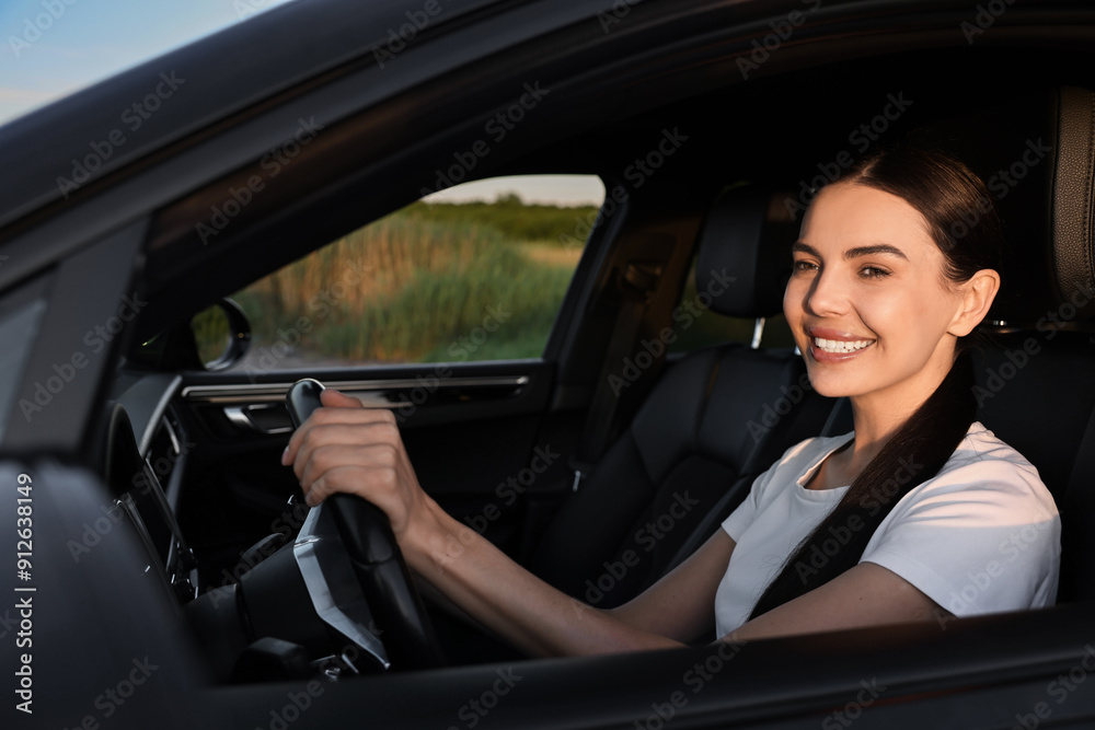 Smiling young woman holding steering wheel while driving car, view from outside Smiling young woman holding steering wheel while driving car, view from outside