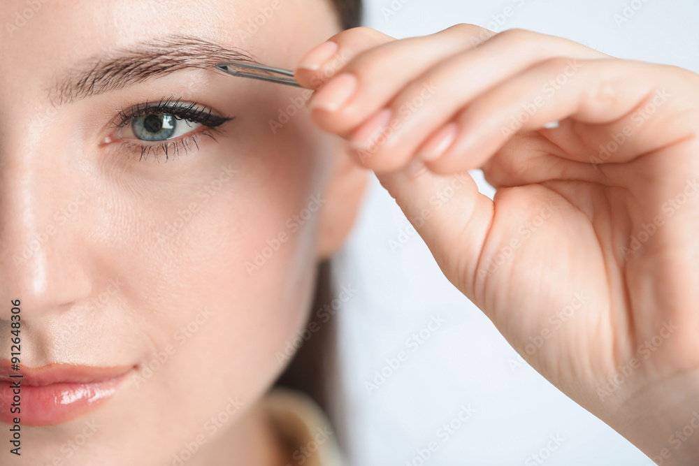Young woman plucking eyebrow with tweezers on light background, closeup Young woman plucking eyebrow with tweezers on light background, closeup