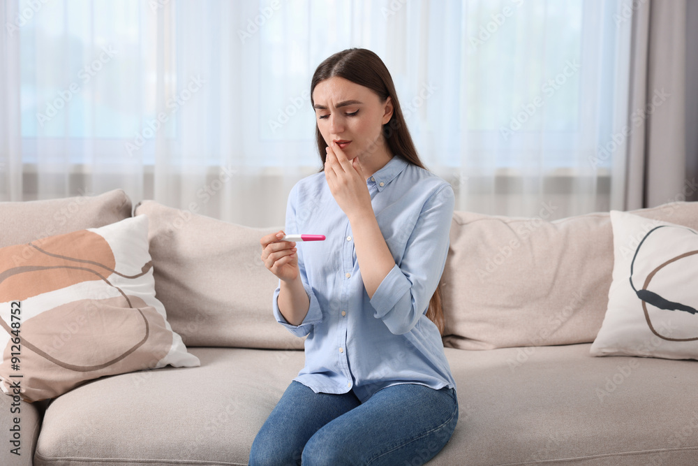 Sad woman holding pregnancy test on sofa indoors Sad woman holding pregnancy test on sofa indoors