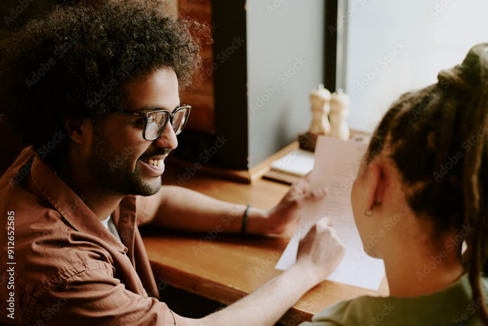 Casual meeting between two people at coffee shop, sharing ideas and reviewing document in hands. Visible papers and coffee cups on wooden table under natural light Casual meeting between two people at coffee shop, sharing ideas and reviewing document in hands. Visible papers and coffee cups on wooden table under natural light