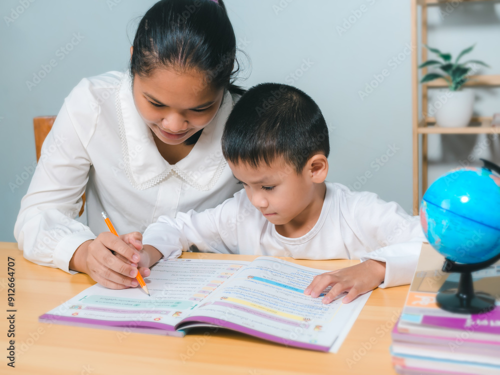 Female tutor helping little elementary school boy with homework during individual lesson at home, Teacher or mother helping boy writing lesson and learning to write, Education home school concept. Female tutor helping little elementary school boy with homework during individual lesson at home, Teacher or mother helping boy writing lesson and learning to write, Education home school concept.