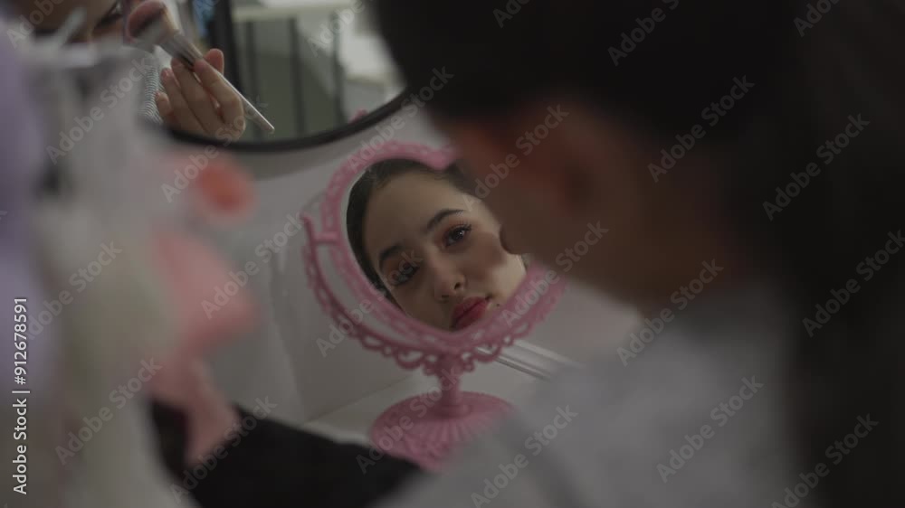 Young woman applying eye makeup at vanity with mirror