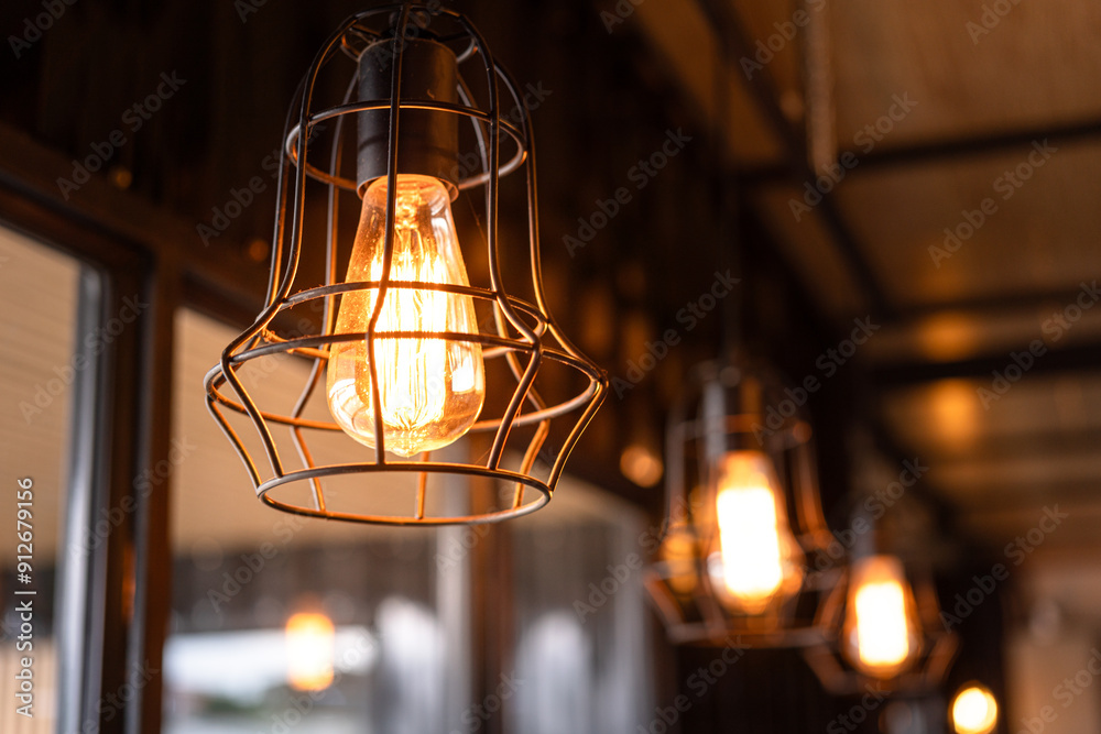 Classic designed ceiling lighting bulb with iron cage, it glowing in orange warm light shade. Object for interior decoration, close-up with selective focus. Classic designed ceiling lighting bulb with iron cage, it glowing in orange warm light shade. Object for interior decoration, close-up with selective focus.