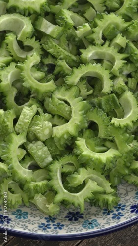 Close-up view of deseeded and sliced raw bitter melon (Momordica charantia) on a plate. Table spin. Vertical video. photo