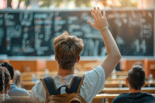 Back view of Caucasian secondary schoolboy rising hand up in school at the lesson. Rear view of male teenager studying in classroom. Back to school