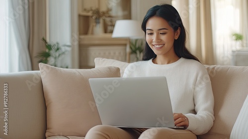 A young woman with long hair smiles at the camera while using a laptop in a beautifully decorated, well-lit living room