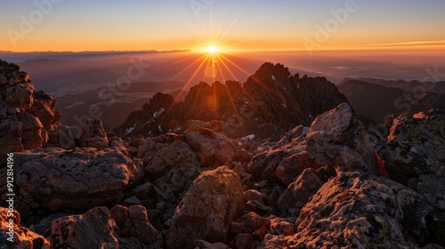 Mountain peak sunrise with sunbeams illuminating rocky landscape.