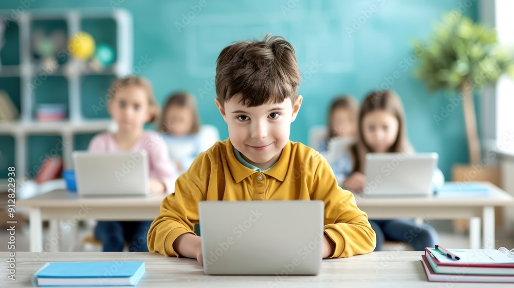 Young boy in a classroom using a laptop during a lesson, with fellow students in the background, focused on learning and education.