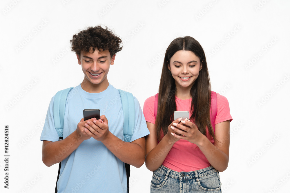 Smiling high school pupils students teenagers classmates boy girl friends bloggers in casual clothes with bags holding smart cell phones using mobile app looking at screen isolated on white background Smiling high school pupils students teenagers classmates boy girl friends bloggers in casual clothes with bags holding smart cell phones using mobile app looking at screen isolated on white background