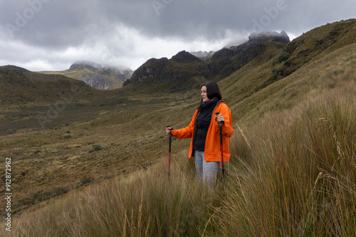 woman in red jacket walking with trekking poles in the middle of the moor with mountains in the background on a cloudy day