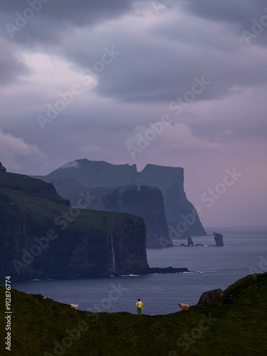 A girl in yellow is standing on a cliff near the kallur lighthouse and enjoying the amazing sunset, Kalsoy, Faroe Island. photo