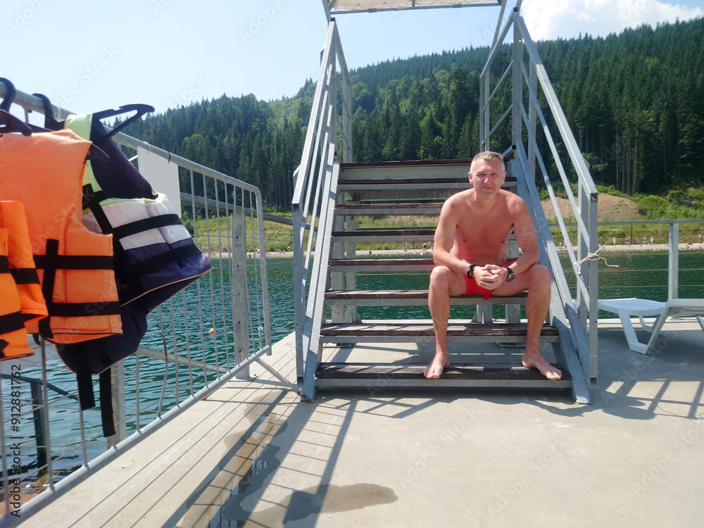 A male beach lifeguard sits on the ladder of a tower.