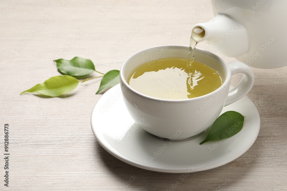 Pouring refreshing green tea into cup at wooden table, closeup Pouring refreshing green tea into cup at wooden table, closeup