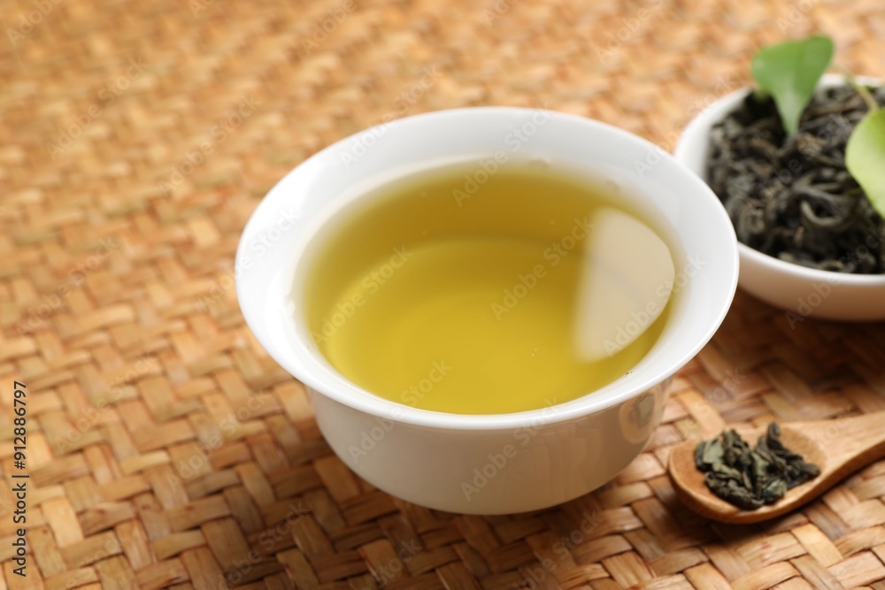 Refreshing green tea in cup, spoon and leaves on table, closeup Refreshing green tea in cup, spoon and leaves on table, closeup