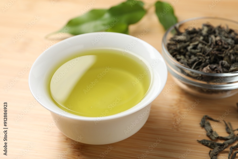 Refreshing green tea in cup and leaves on wooden table, closeup Refreshing green tea in cup and leaves on wooden table, closeup